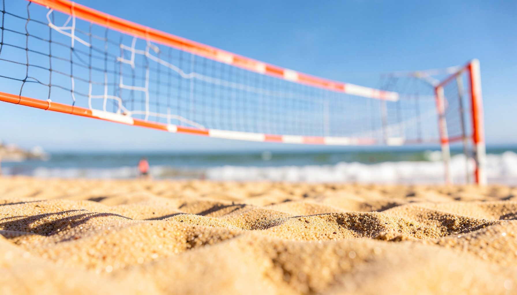 Güneşli bir plaj voleybolu sahası; altın rengi kum, turuncu-beyaz voleybol filesi, açık mavi gökyüzü ve yumuşak dalga köpükleriyle sakin bir yaz atmosferi