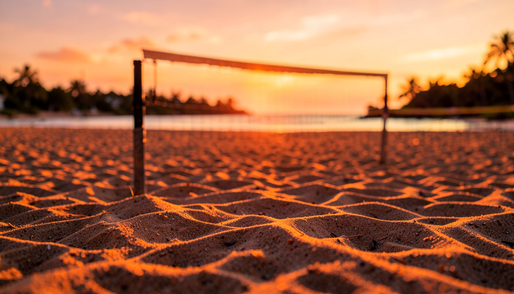 Florida'da geniş bir kum saha üzerinde voleybol filesi, turuncu ve altın rengi gün batımı ışığıyla aydınlanan sakin bir plaj atmosferi